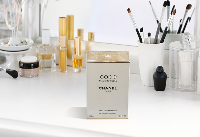 Ein Parfüm steht verpackt vor einem Spiegel, im Hintergrund sind weitere Parfüme