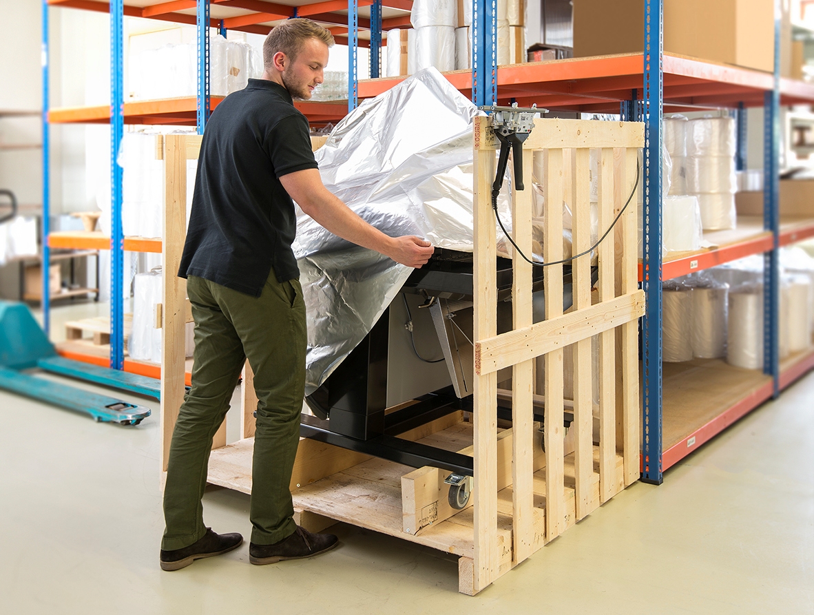 Eine Maschine wird für den Transport vorbereitet, ein Mann zieht eine Alufolie über die Maschine.