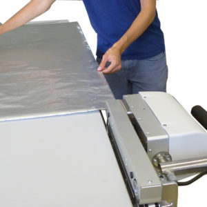 Mit einem Durchlaufsiegelgerät, das am Tisch befestigt ist, wird ein Verbundmaterial gesiegelt, das auf dem Tisch liegt