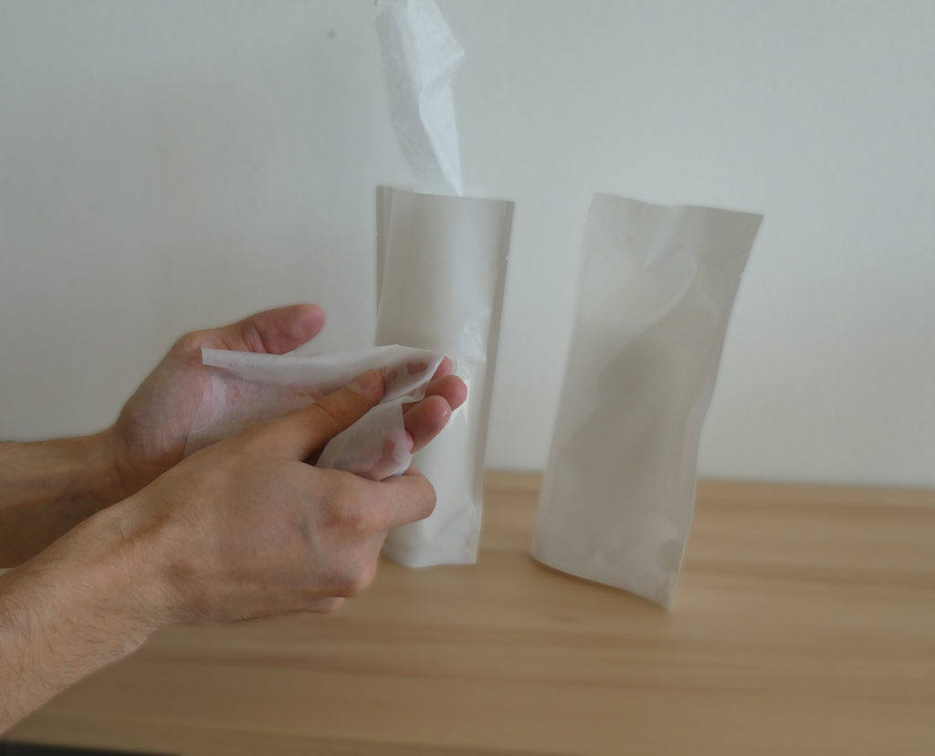 Ein Mensch benutzt ein Desinfektionstuch, die Verpackung der Desinfektionstücher steht im Hintergrund.