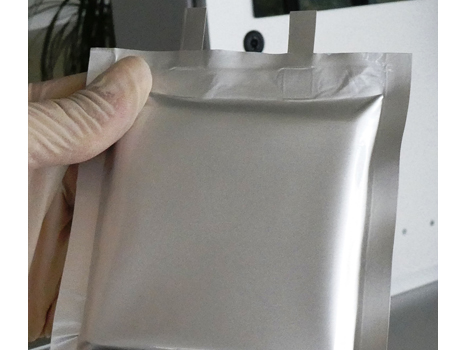 Pouch Zelle aus der Batterieforschung, die vor einem Laborsiegelgerät gehalten wird.