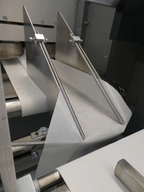 Detailaufnahme einer horizontalen Schlauchbeutelmaschine. Zu sehen ist, wie das Spezialpapier über eine Formschulter in die Maschine befördert wird und dort versiegelt wird.