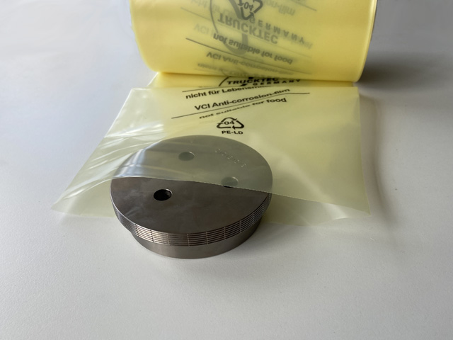 Ein Ersazteil aus Metall ragt zur Hälfte aus einem gelben VCI-Beutel.