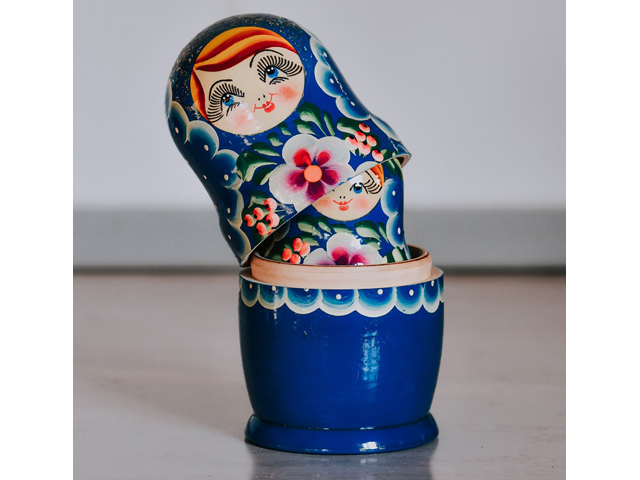 Eine Matryoschka-Puppe vor einem grauen Hntergrund. Die Puppe ist leicht geöffnet und im Inneren ist die kleinere Puppe zu sehen.